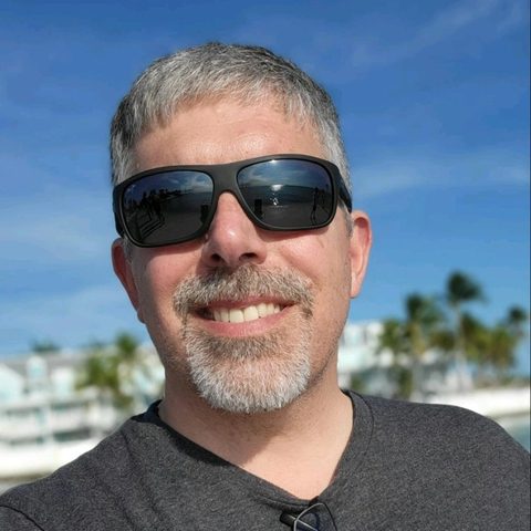 Randy Hinders, smiling outdoors in sunglasses under a blue sky.